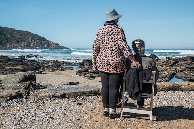 resident in wheelchair and carer at beach looking at waves
