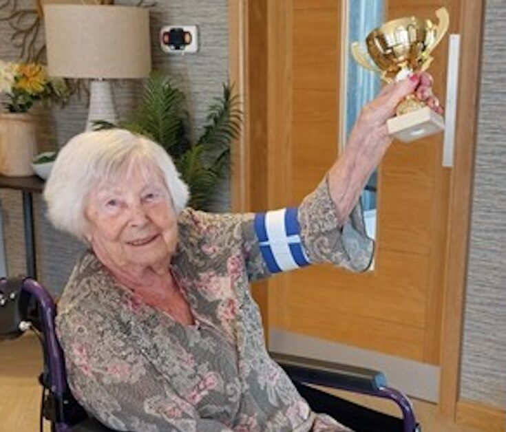 one of our residents sat holding her sports day trophy smiling