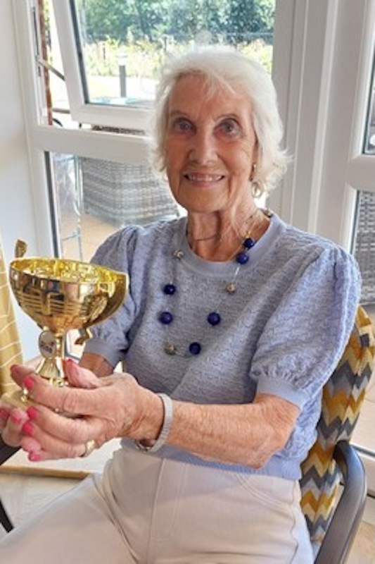 one of our residents sat holding her sports day trophy smiling