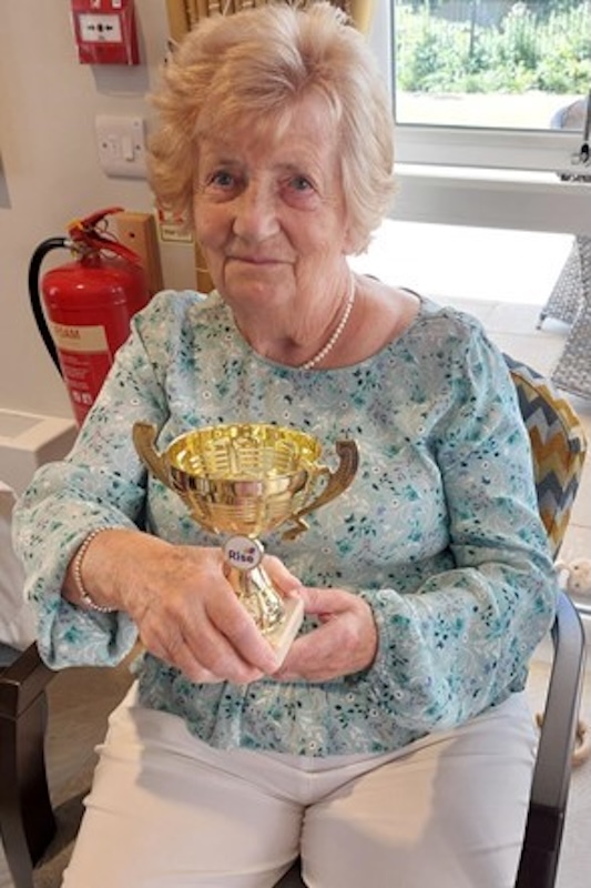 one of our residents sat holding her sports day trophy smiling