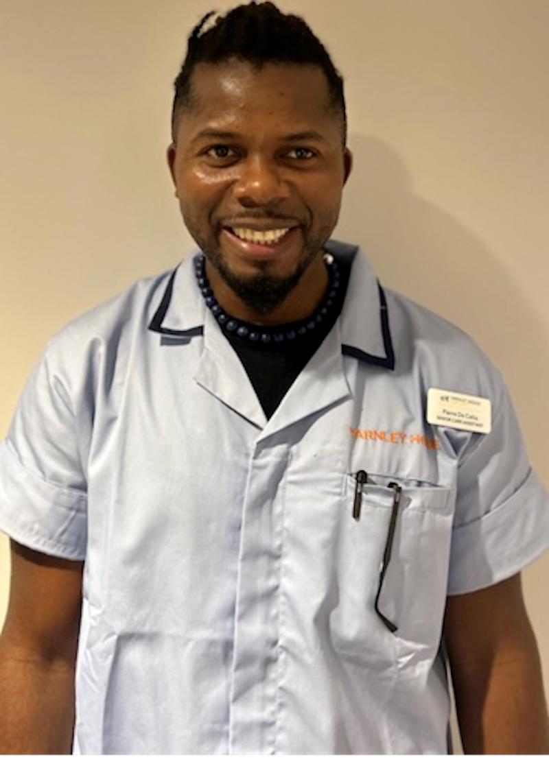 man with black hair wearing a carers uniform having his headshot taken for the team page