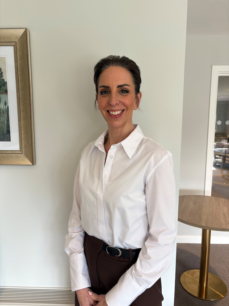woman with brown hair wearing a white shirt smiling having her photo taken for the team page