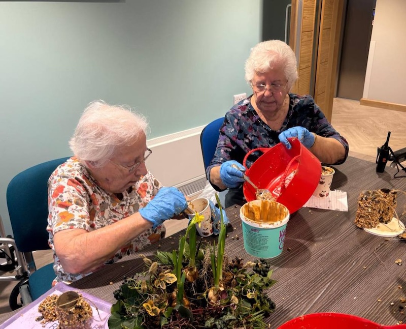 2 female residents sat down at a table making bird feeders with peanut butter