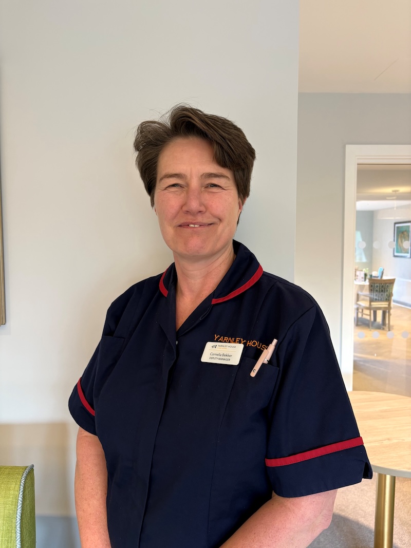 woman with brown hair wearing a navy nurse uniform smiling having her photo taken for the team page