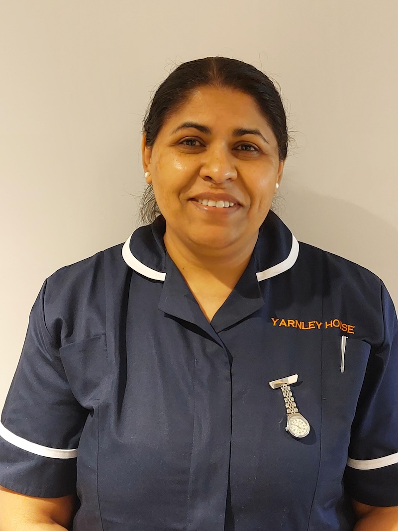 woman with brown hair wearing a navy nurse uniform smiling having her photo taken for the team page