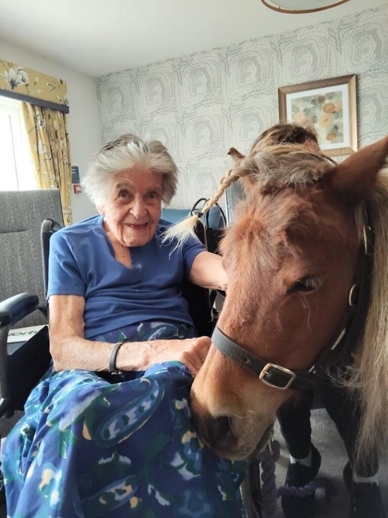 female resident wearing blue sat down stroking a therapy pony