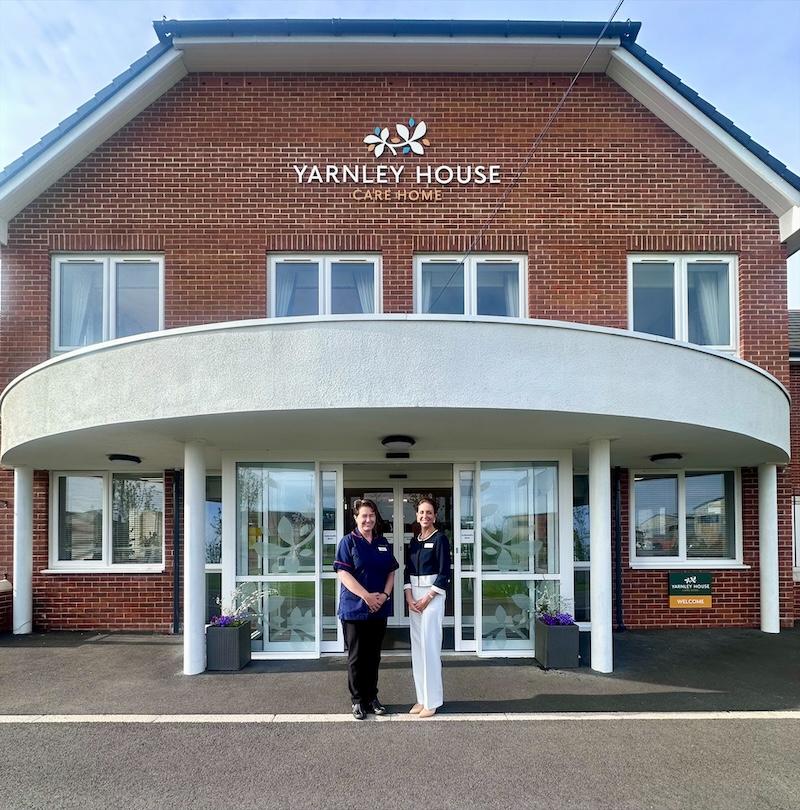 the manager and deputy manager at yarnley house stood outside the entrance of the home smiling