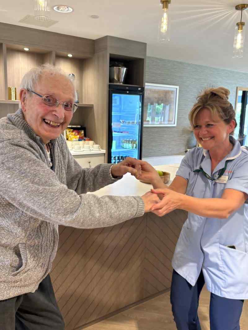 resident and carer stood smiling and holding hands